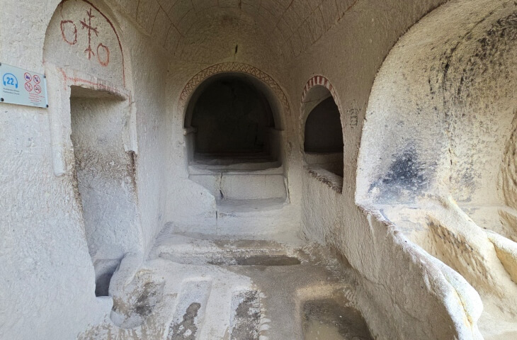 Göreme Açık Hava Müzesi’ndeki Pantokrator Kilisesi’nin iç mekanı, kaya oyma mimari ve kırmızı haç motifleriyle süslenmiş duvarlarıyla görülüyor.